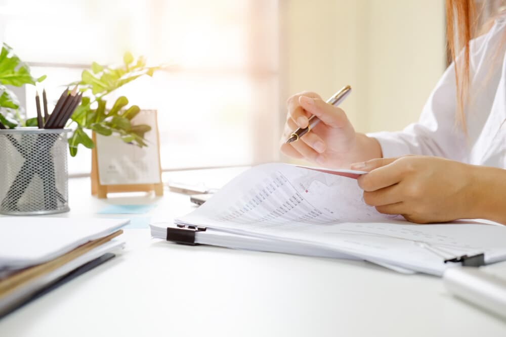 Hände mit Finanzunterlagen und Stift an einem hellen Schreibtisch